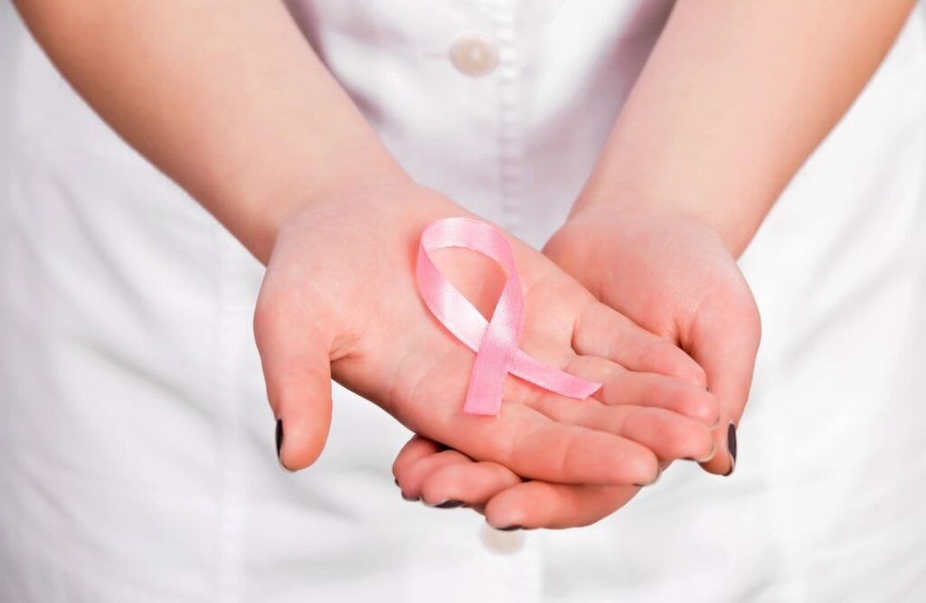 Hands cupped together holding a pink ribbon, symbolizing breast cancer awareness.