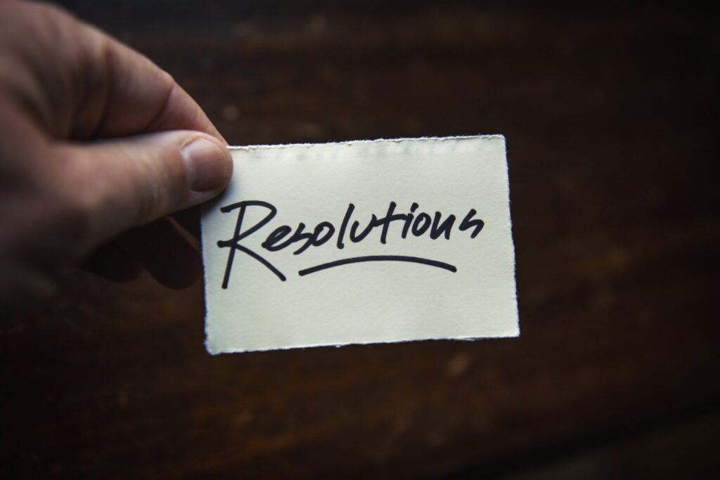 A hand holding a small piece of paper with the word "Resolutions" handwritten in black ink.