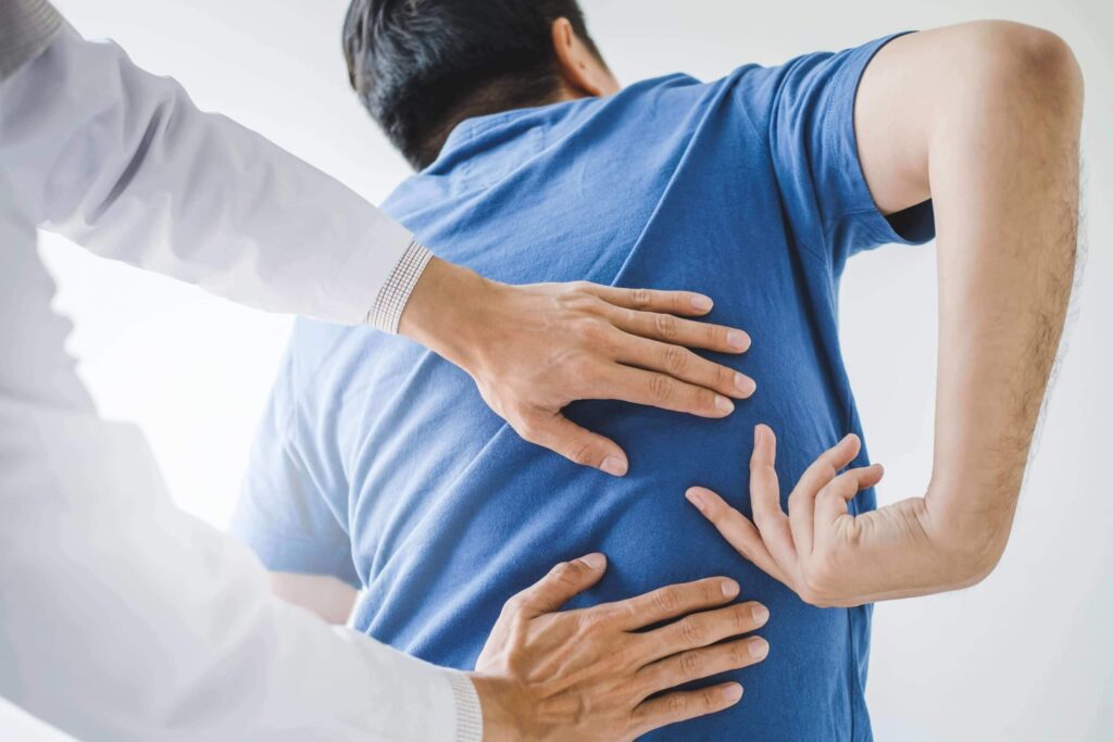 Physical therapist examining a patient's back, both wearing casual attire, in a bright clinical setting.