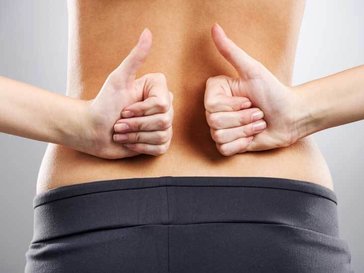 Close-up of a person's lower back with two thumbs up on either side, indicating a pain-free back.