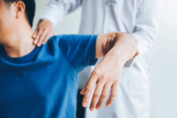 A physical therapist examining a patient's shoulder and arm in a clinical setting.