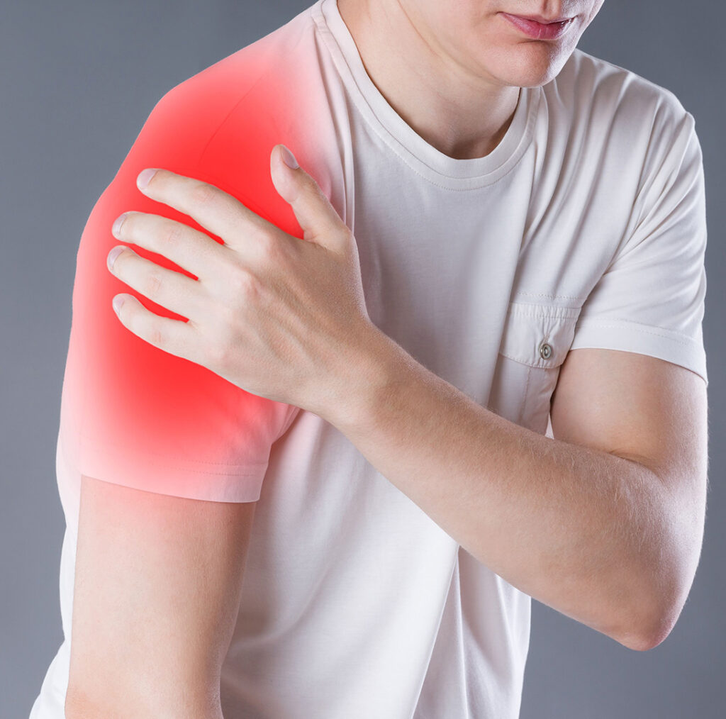 A person wearing a white t-shirt holding their shoulder in pain, with a red highlighted area indicating discomfort or injury.