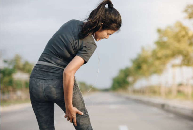 A girl bending forward with one hand on their knee and the other on their lower back, standing on an empty road, apparently in discomfort or fatigue.