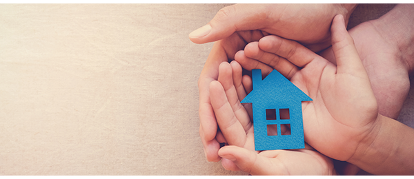 Adult and child hands holding a small blue paper cutout of a house.