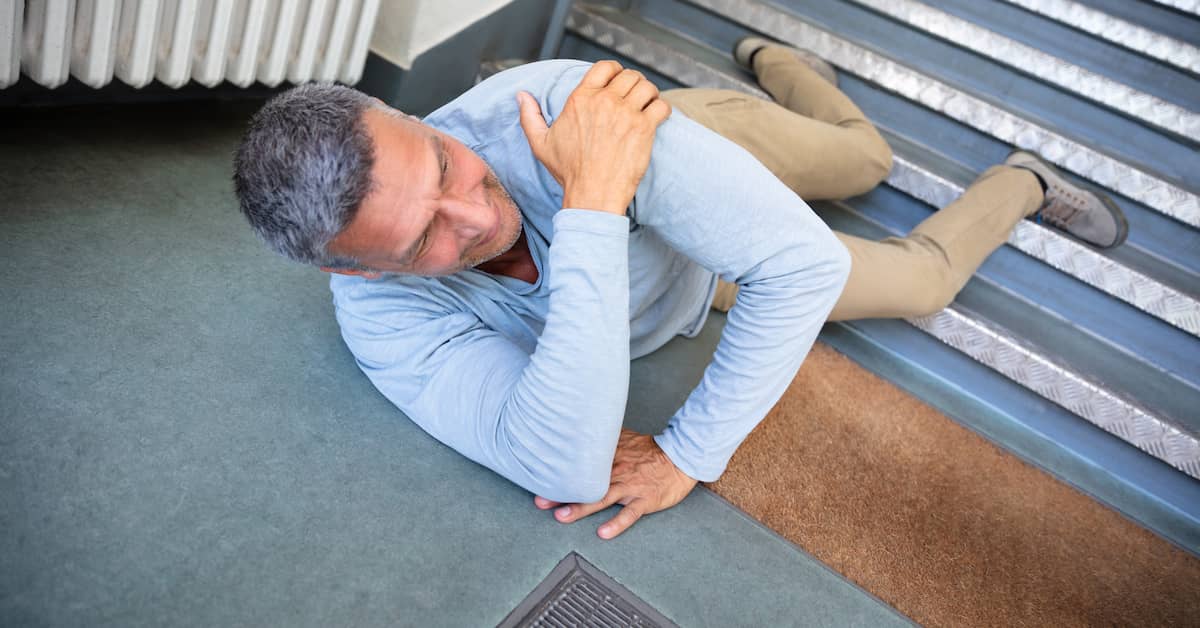 A person in a light blue shirt and beige pants is crouched down on carpeted stairs with a hand clasping their head, appearing to be in distress.